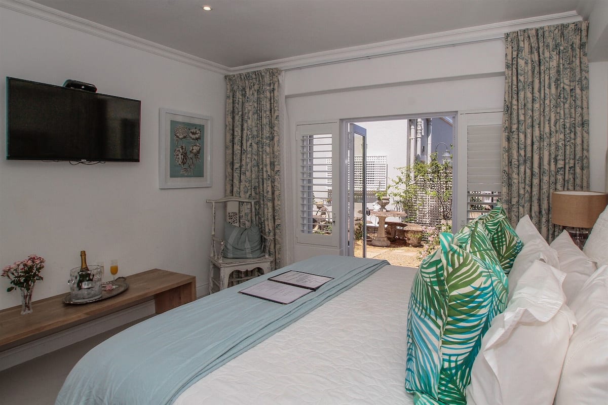 Ein Hotelzimmer mit Bett, Fernseher, Schreibtisch mit Vase und Flasche sowie Blick nach draußen.