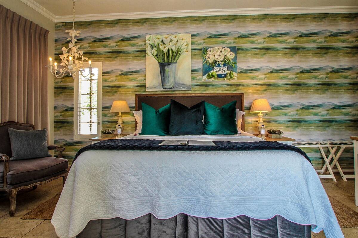 Ein Schlafzimmer mit einem großen Bett, zwei Nachttischlampen, einer Deckenleuchte, einem Sessel und einem Fenster mit Vorhängen.