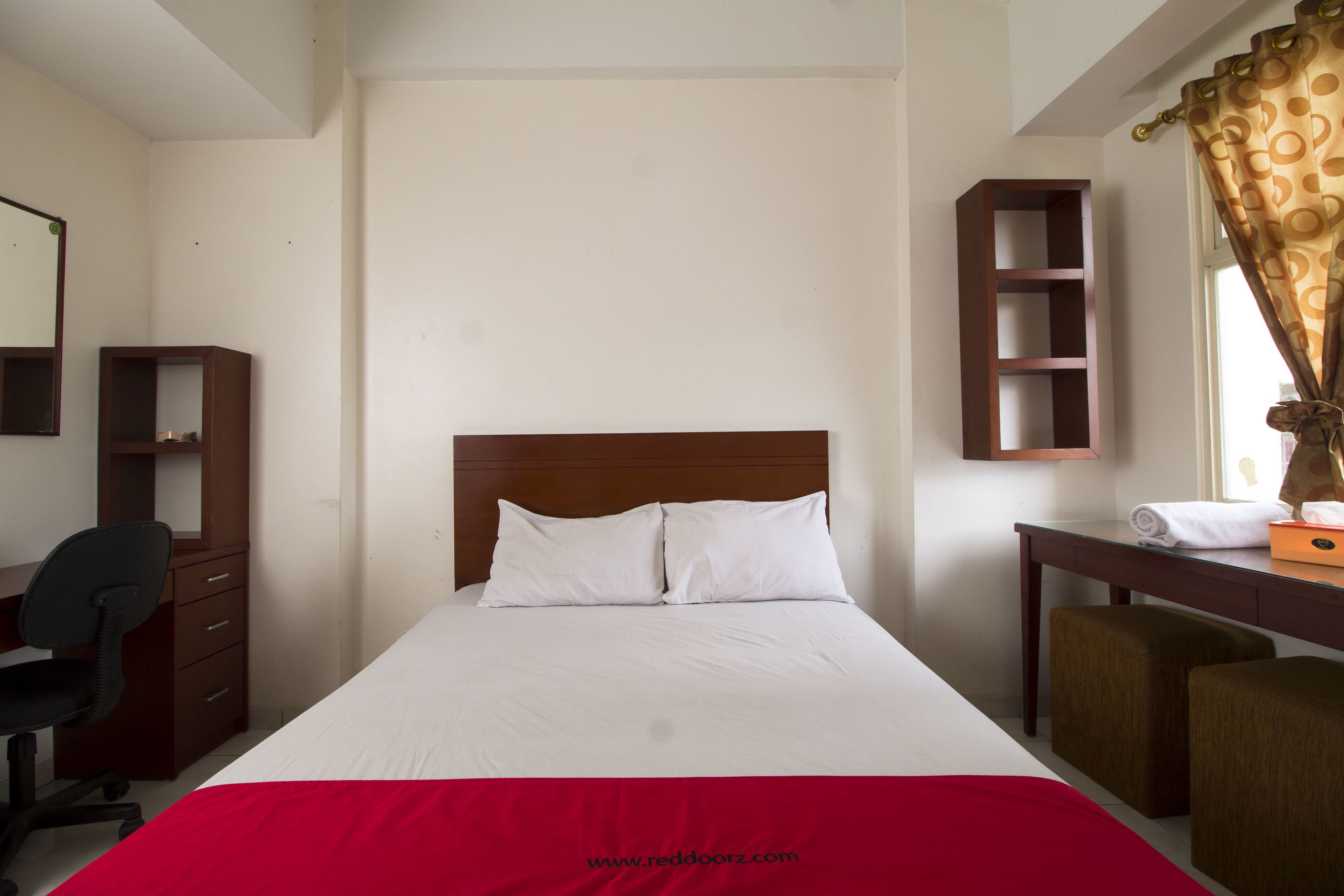 Una habitación de hotel con cama, escritorio, silla, armario y estante.
