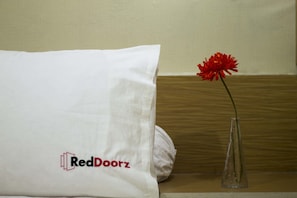Un lit avec un oreiller blanc et un vase transparent contenant une fleur rouge.