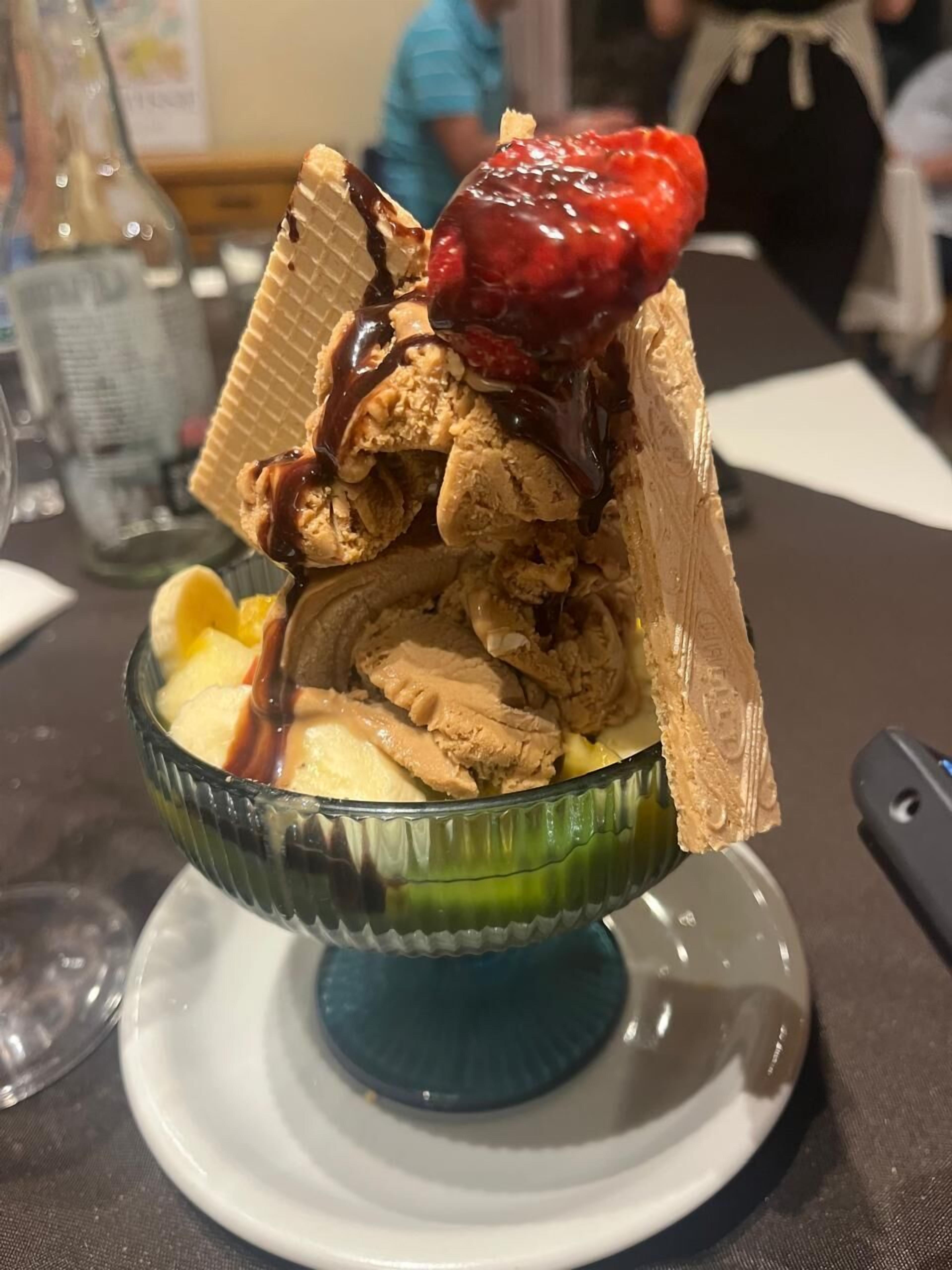 Un postre con helado, fruta y salsa de chocolate en un bol de vidrio sobre un plato.