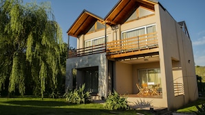 A modern two-story house with a balcony, large windows, and a well-maintained garden. - Posada y Spa Las Golondrinas (Villa La Arcadia)