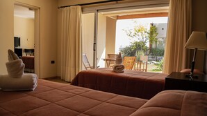 A hotel room with two beds, a balcony with a table and chairs, and a TV in the corner. - Posada y Spa Las Golondrinas (Villa La Arcadia)
