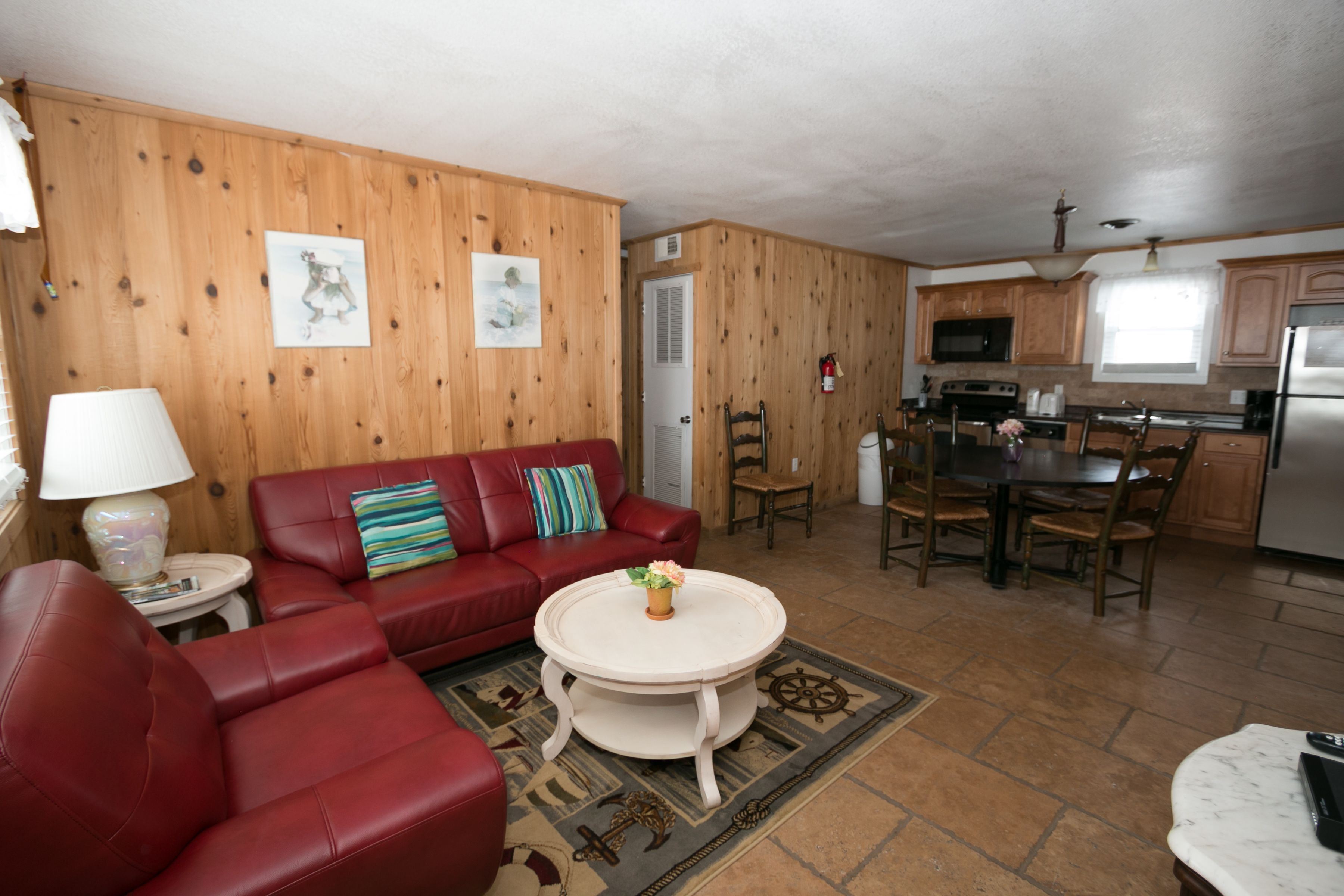 A living room with a red leather sofa, a round coffee table, and a dining area with wooden chairs and a table.