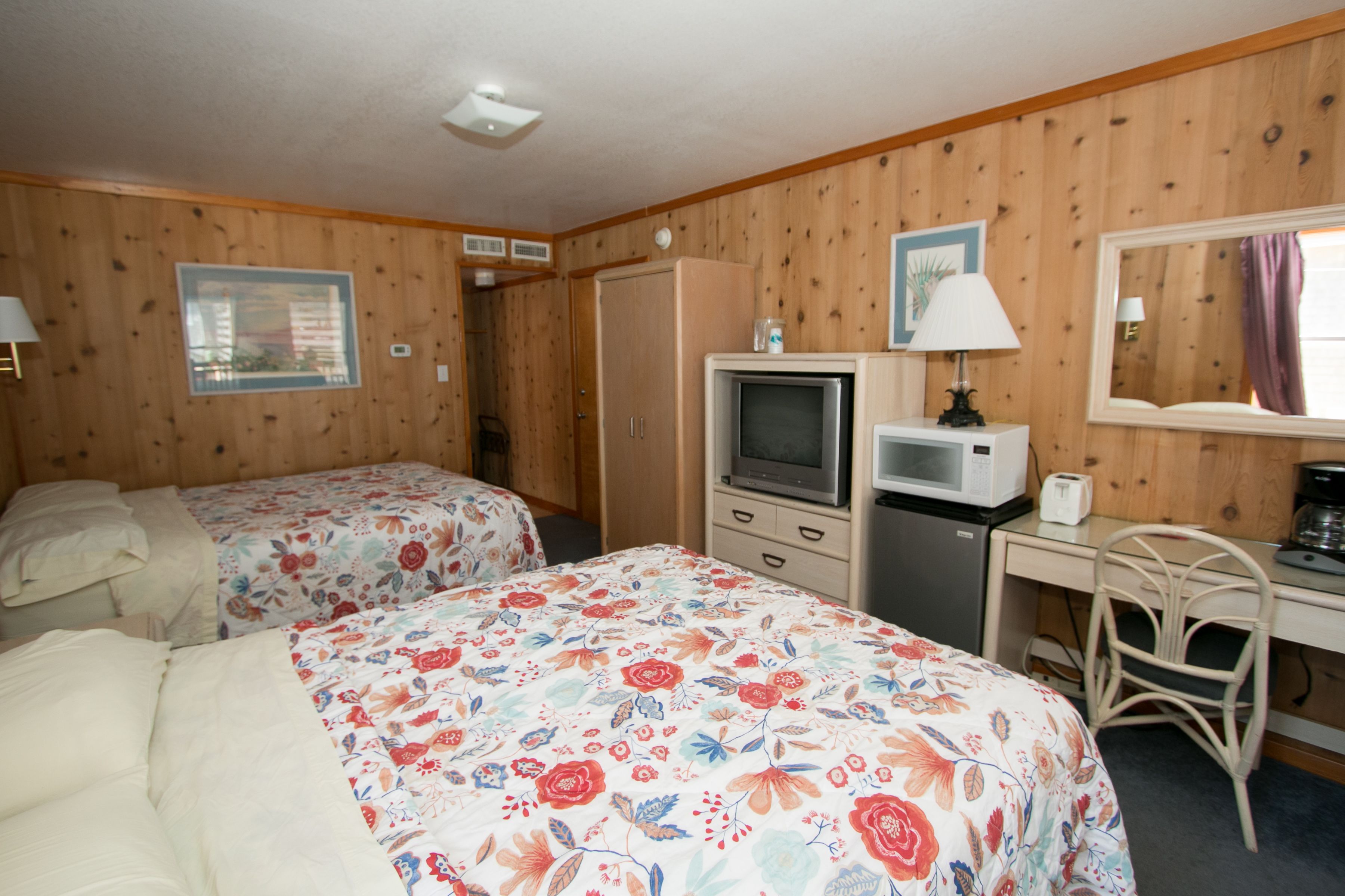 A room with two beds, a desk, a chair, a television, and a microwave.