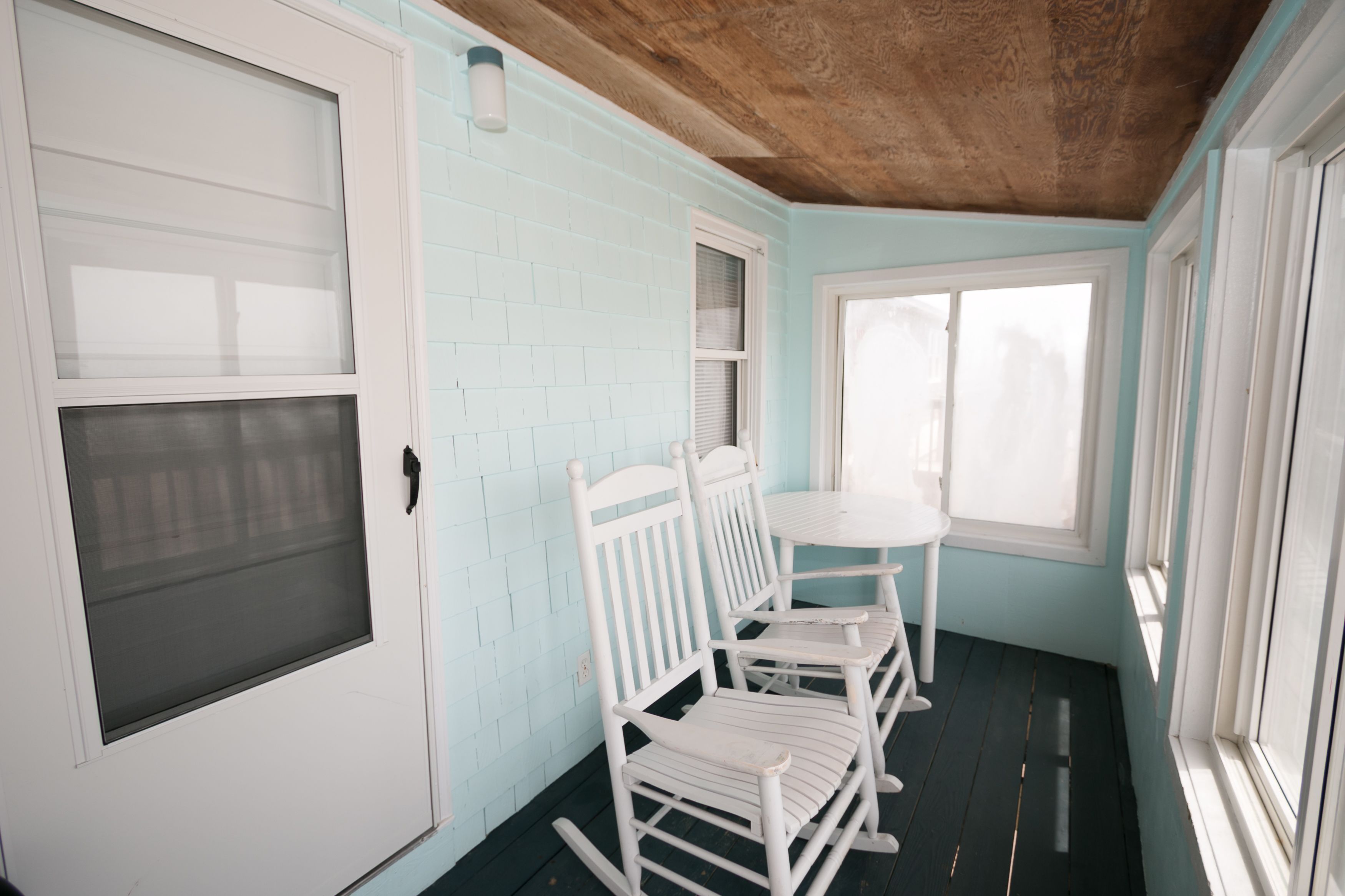 Ein Zimmer mit Holzboden, hellblauen Wänden, einer weißen Tür und einem Fenster mit Jalousien.