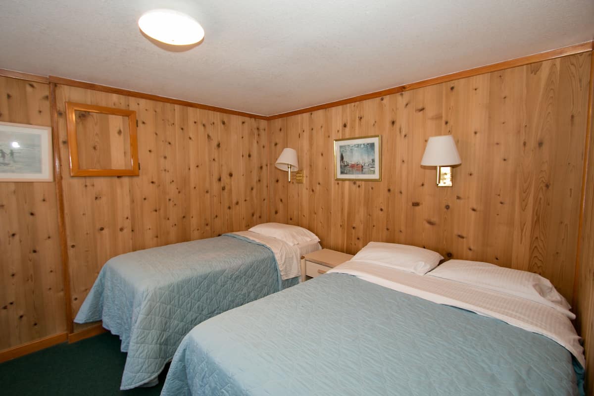 Quarto com duas camas, paredes de madeira e duas luminárias na parede.