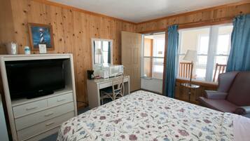 Quarto com cama, televisão, escrivaninha, cadeira e janela com cortinas.