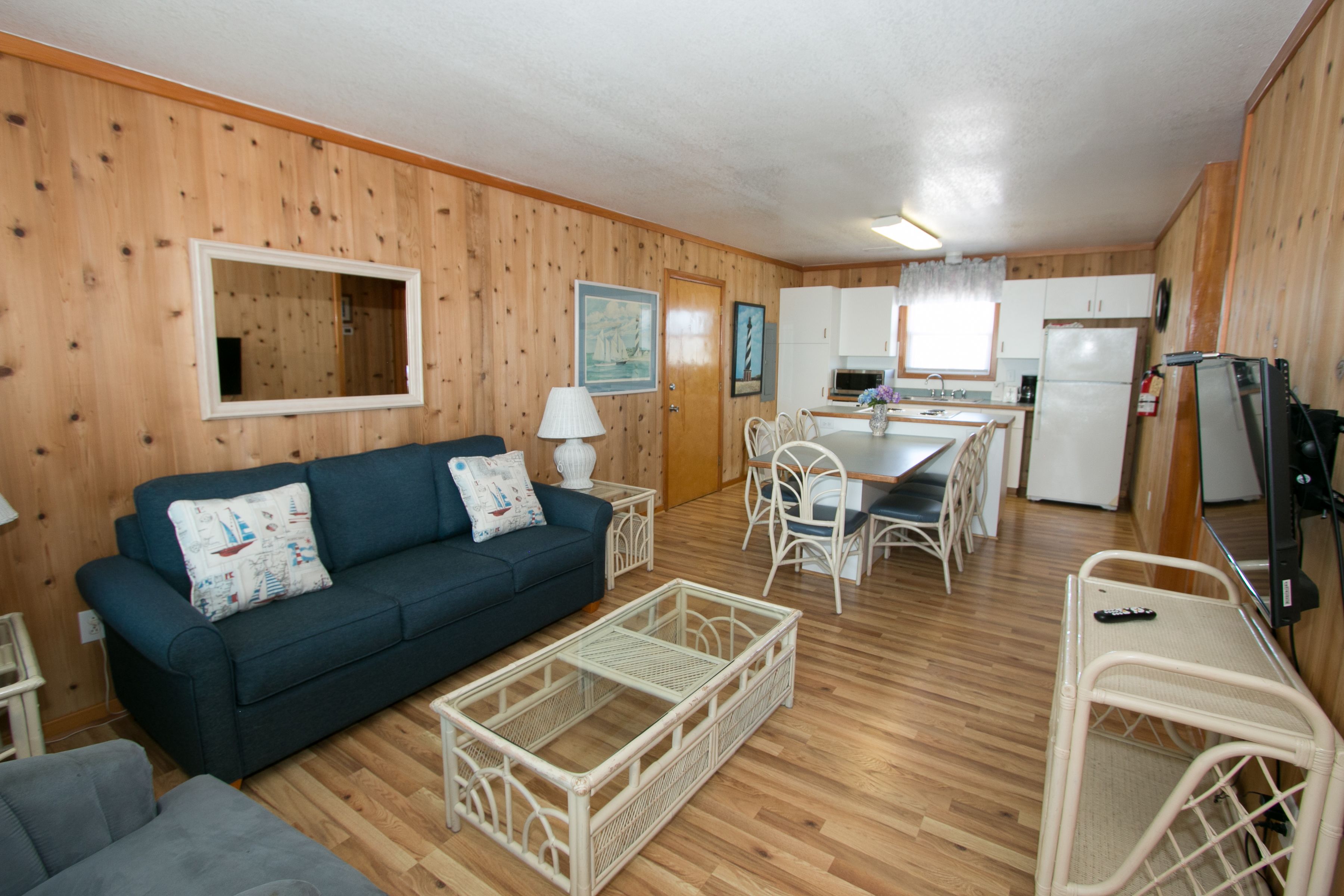 A compact living space with a dark blue sofa, a white wicker coffee table, a dining table with chairs, and a kitchenette area.
