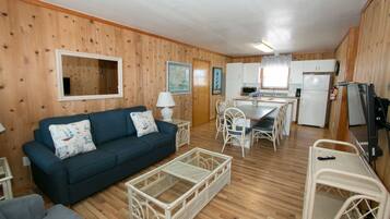 A compact living space with a dark blue sofa, a white wicker coffee table, a dining table with chairs, and a kitchenette area.
