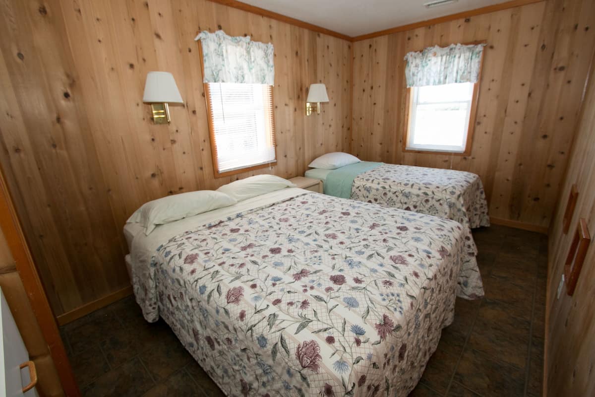Quarto com duas camas, paredes de madeira e duas janelas com cortinas.