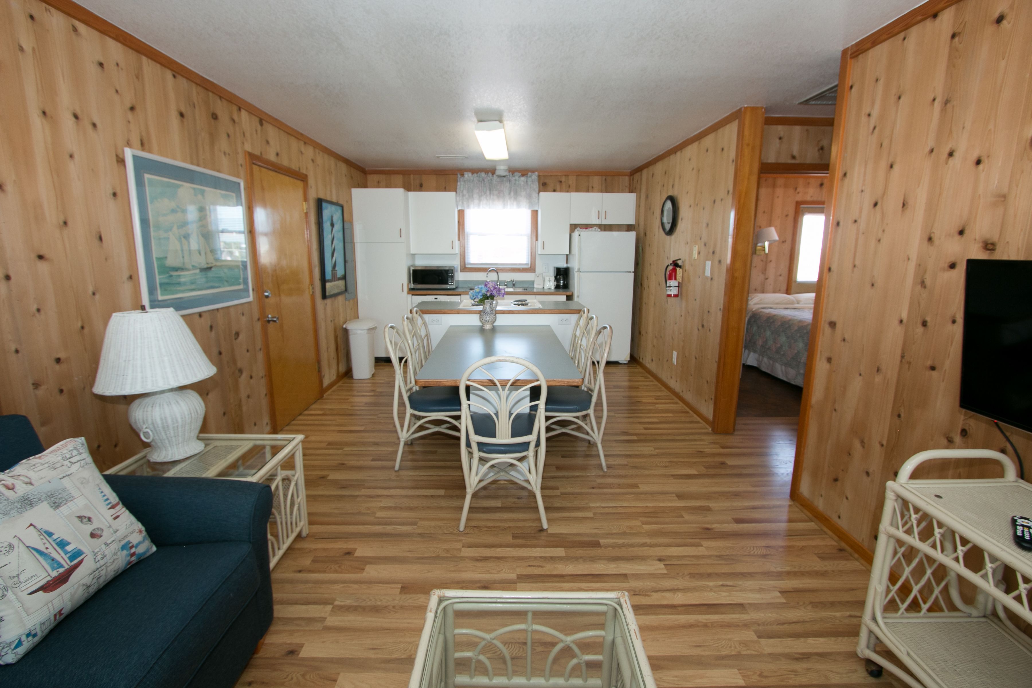 A compact room with a dining table, chairs, a sofa, a TV, and a kitchenette.
