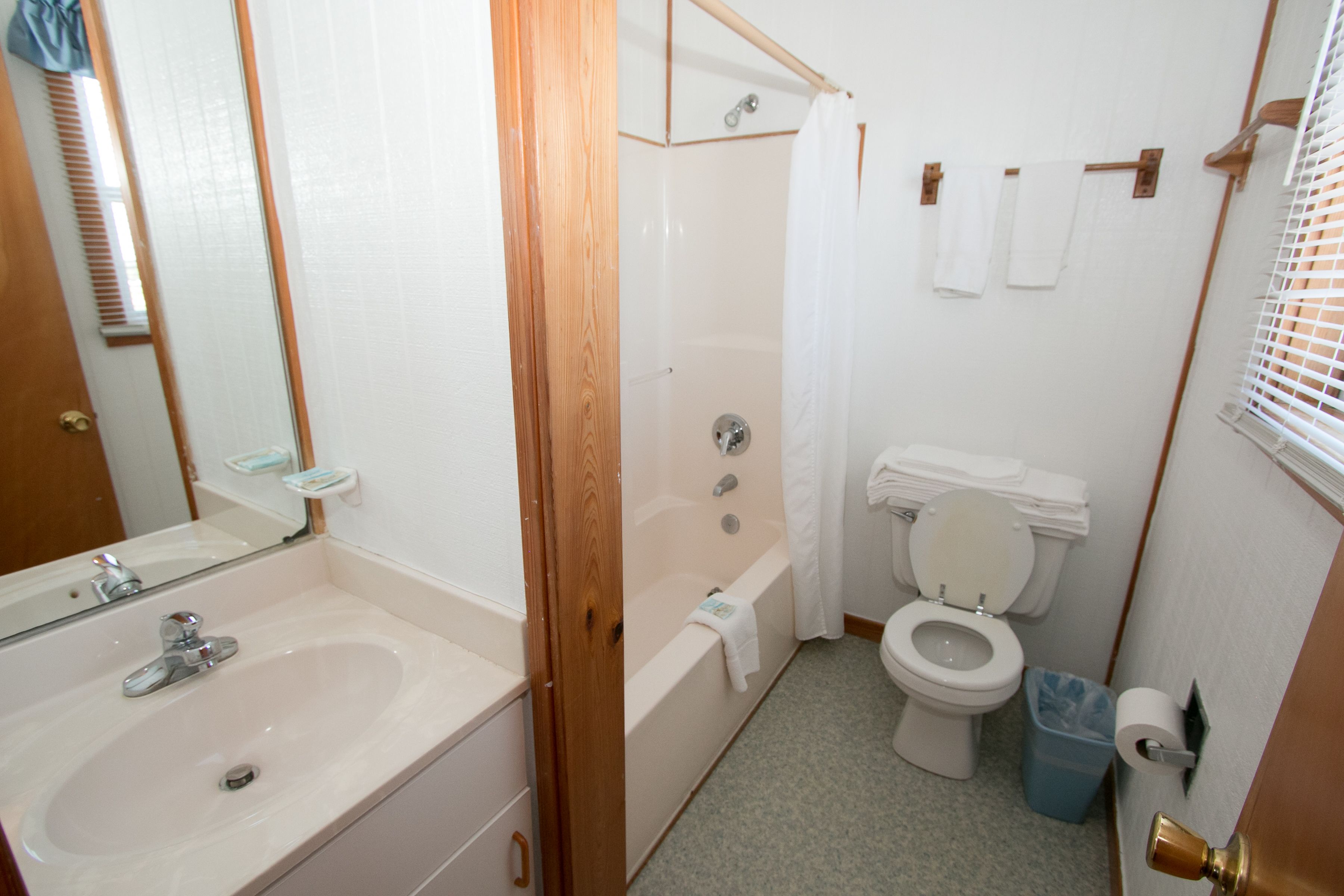 Et badeværelse med vask, badekar, toilet og bruseforhæng.