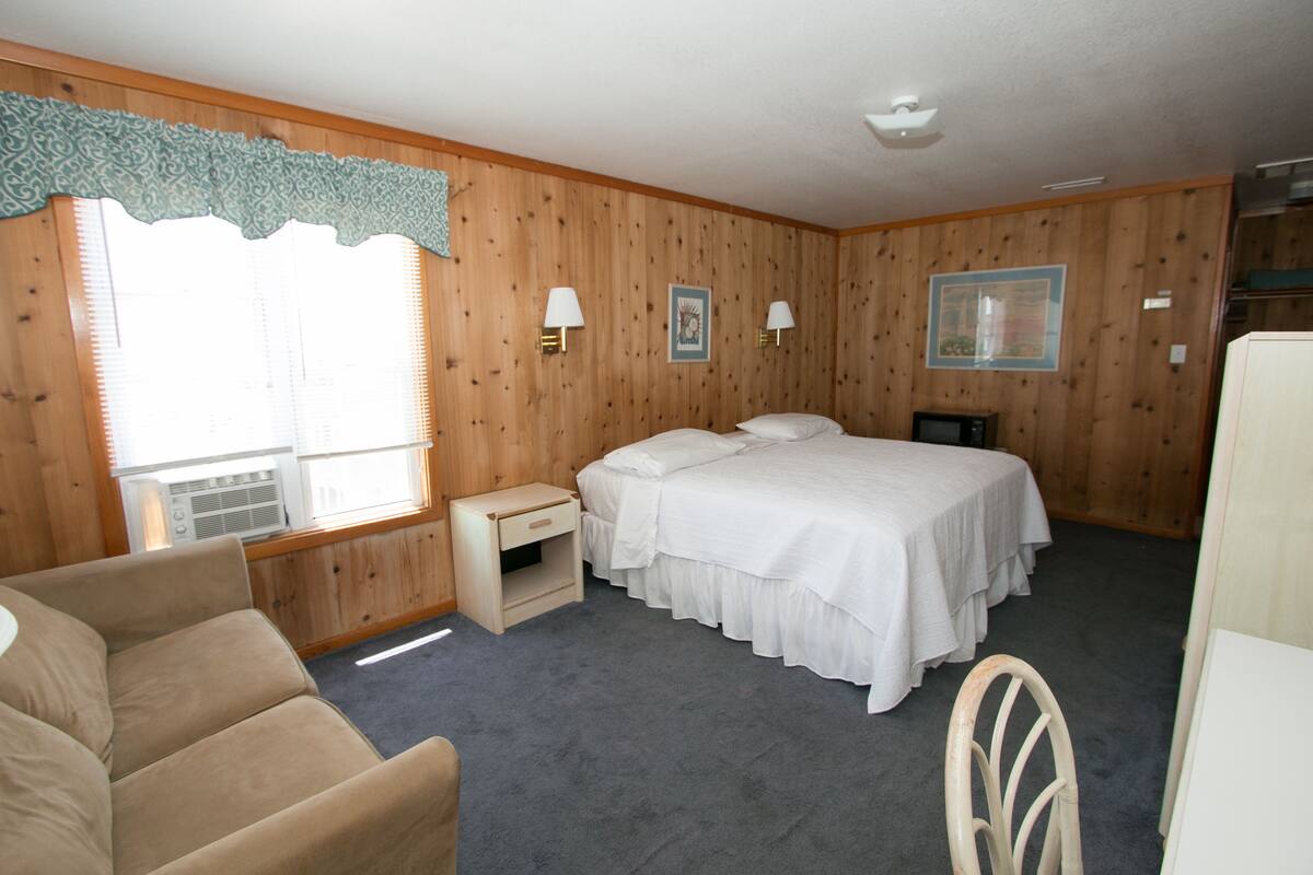 Quarto com cama, duas mesas de cabeceira, uma cadeira e janela com persianas.