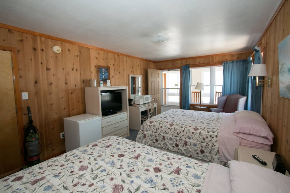 Quarto com duas camas, uma escrivaninha com computador, televisão e janela com cortinas.
