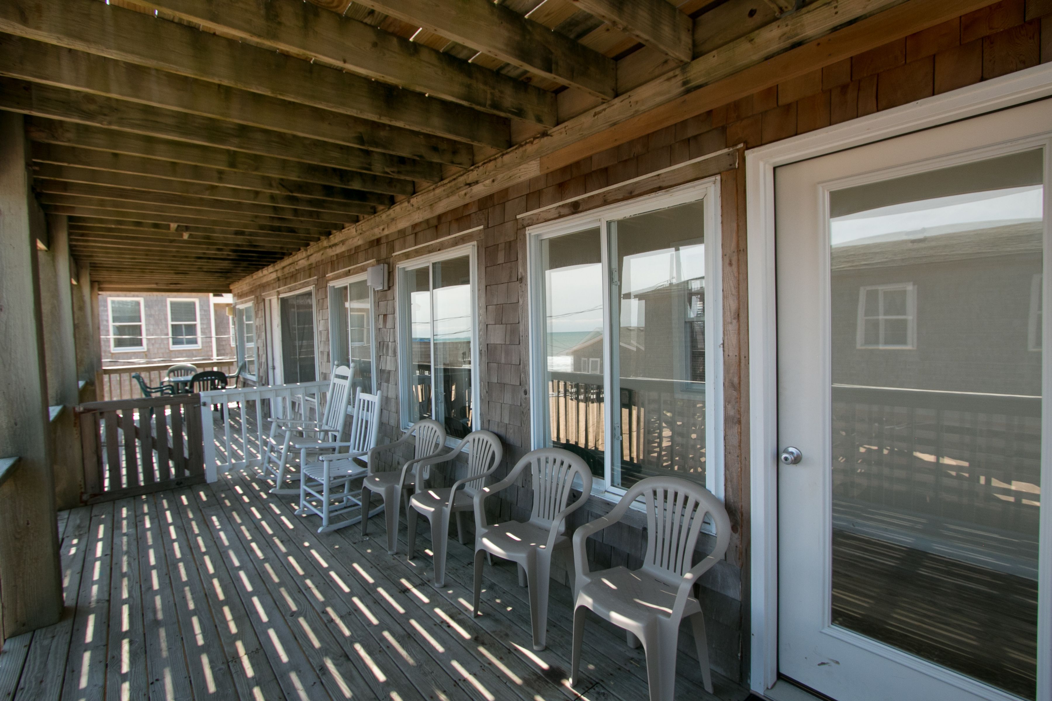 A covered porch with wooden flooring and white plastic chairs.