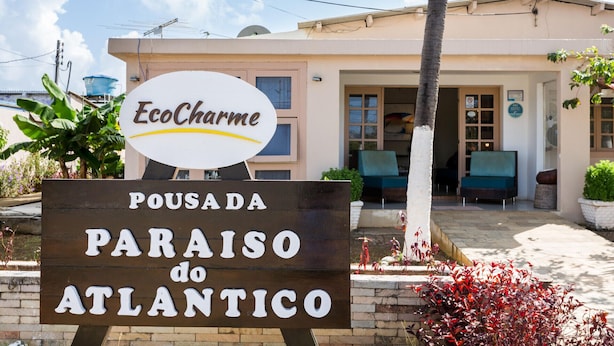 Schild für EcoCharme Pousada do Atlantico, das ein Hotel mit Außenbereich und Blick auf den Haupteingang zeigt.