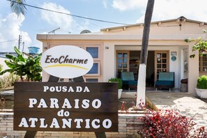 Skilt for EcoCharme Pousada do Atlantico, der viser et hotels miljø med udendørs siddepladser og udsigt til bygningens indgang.