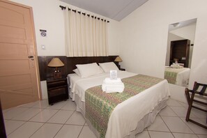 A hotel room with a bed, a nightstand, a lamp, a mirror, and a door.