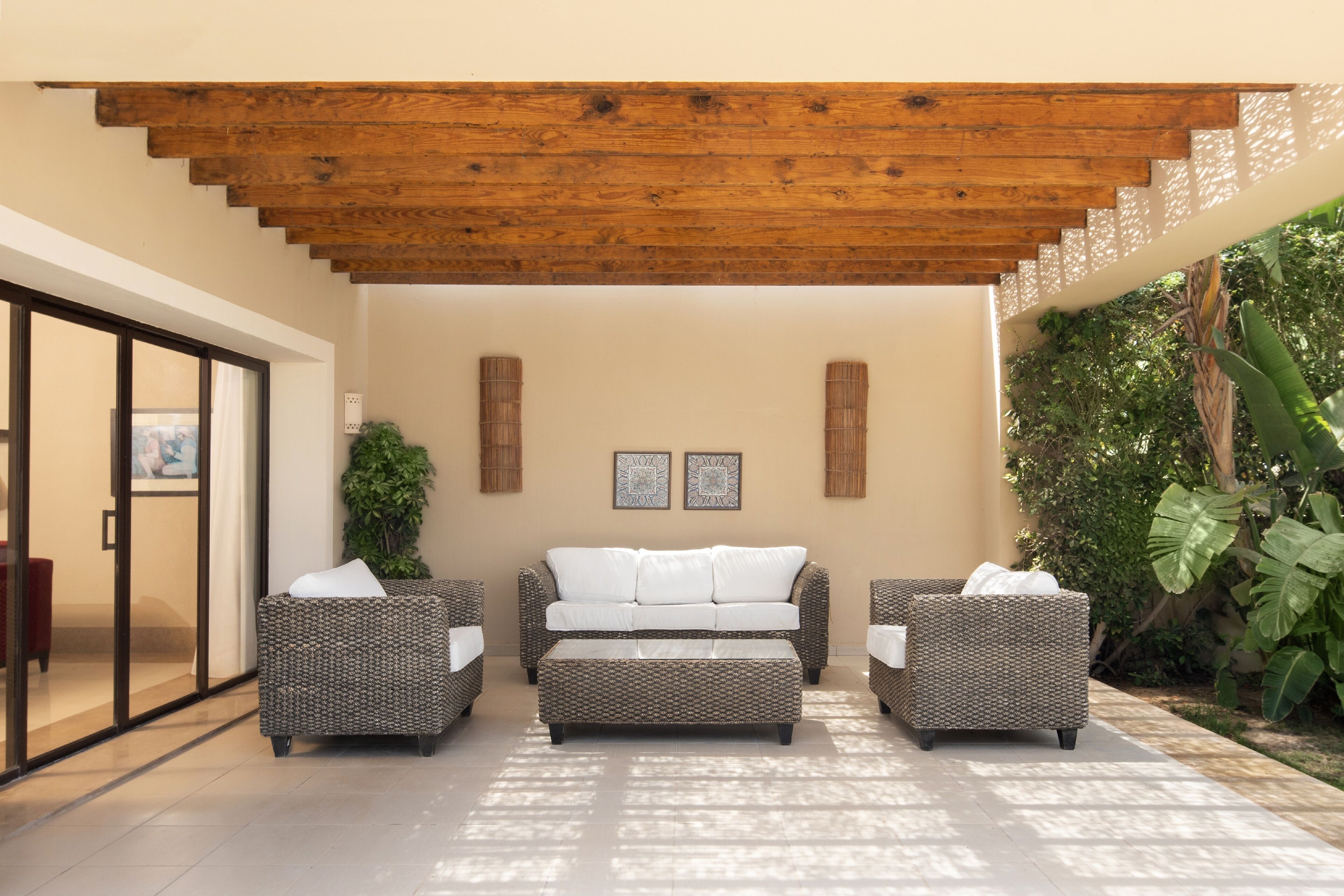 Un área de estar exterior moderna con techo de madera, pared color beige y una planta grande.