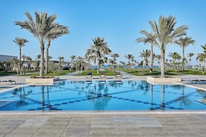 A swimming pool with palm trees and lounge chairs, surrounded by a well-maintained lawn and a clear blue sky. - JAZ Oriental, Almaza Bay (Marsa Matrouh)