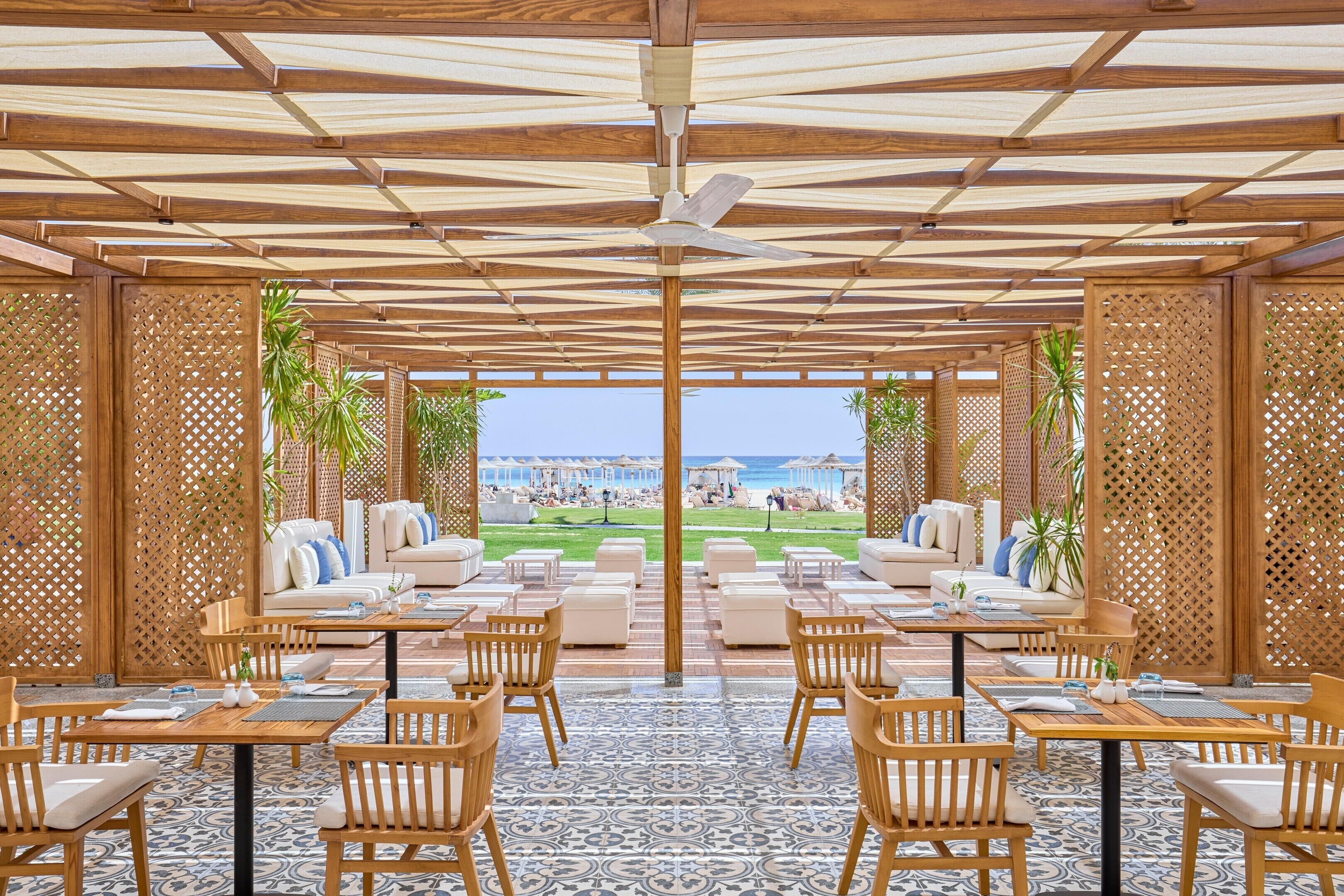 A covered outdoor seating area with wooden furniture and a view of the beach.