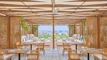 A covered outdoor seating area with wooden furniture and a view of the beach.