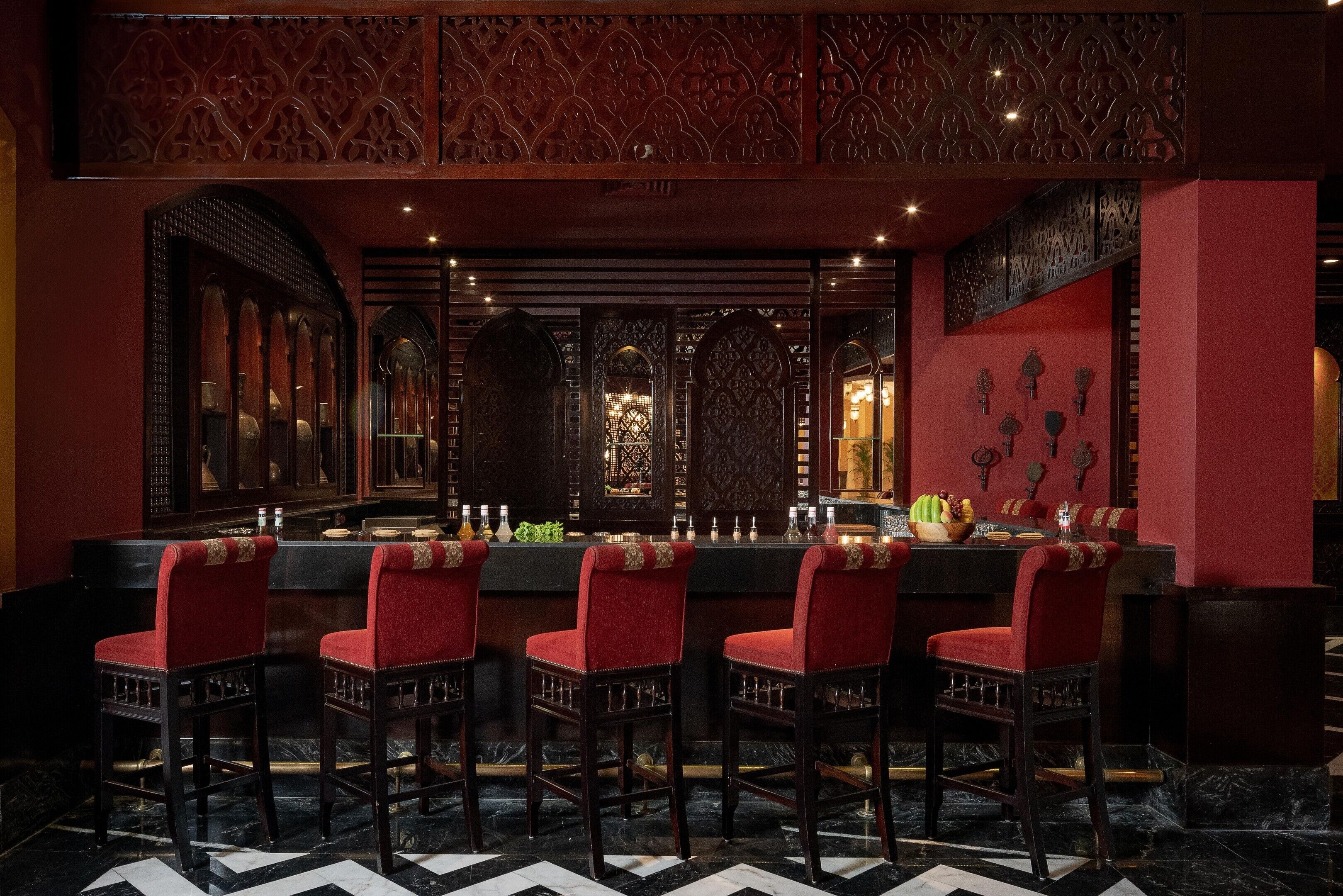 A bar area with a checkered floor, red upholstered chairs, and a bar counter with bottles and glasses.