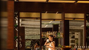 Zona de bar con suelo a cuadros, taburetes y una mujer sentada en uno.