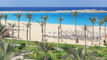 A beach resort with a sandy beach, palm trees, and umbrellas.