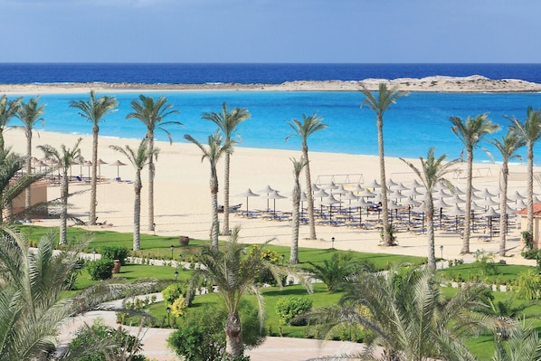 A beach resort with a sandy beach, palm trees, and umbrellas.