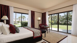 Amplia habitación de hotel con una cama grande, una zona de estar con una silla y una mesa, y ventanas amplias que ofrecen vistas al exterior.