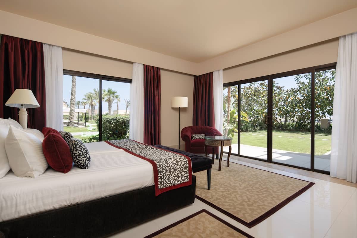 Ein geräumiges Hotelzimmer mit einem großen Bett, einer Sitzecke mit Stuhl und Tisch und großen Fenstern mit Blick ins Freie.