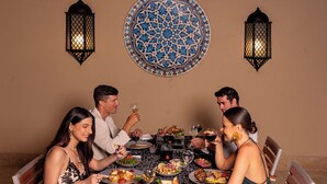Una mesa de comedor con mantel estampado, rodeada de sillas, y un tapiz decorativo sobre ella.