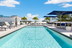 A swimming pool with lounge chairs and umbrellas, surrounded by palm trees and modern architecture. - H2O Suites - Adults Only (Key West)