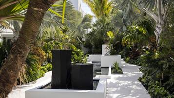 A modern outdoor garden with a water feature, white planters, and lush tropical plants.