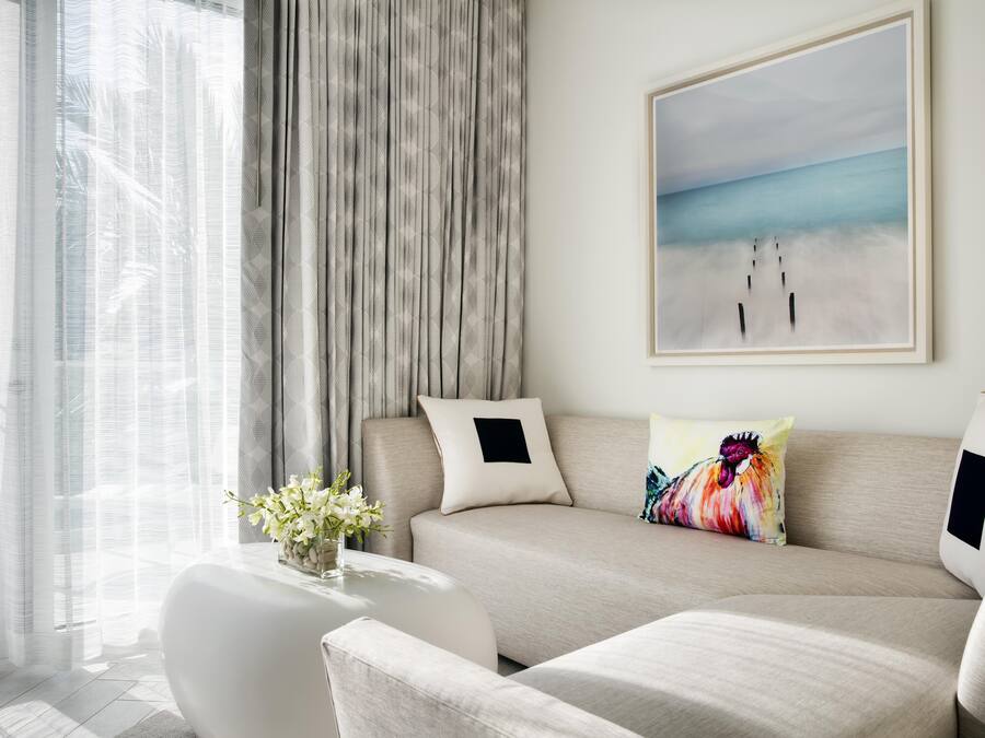 A modern living room with a sofa, a coffee table with a vase of flowers, and a painting of a beach scene.