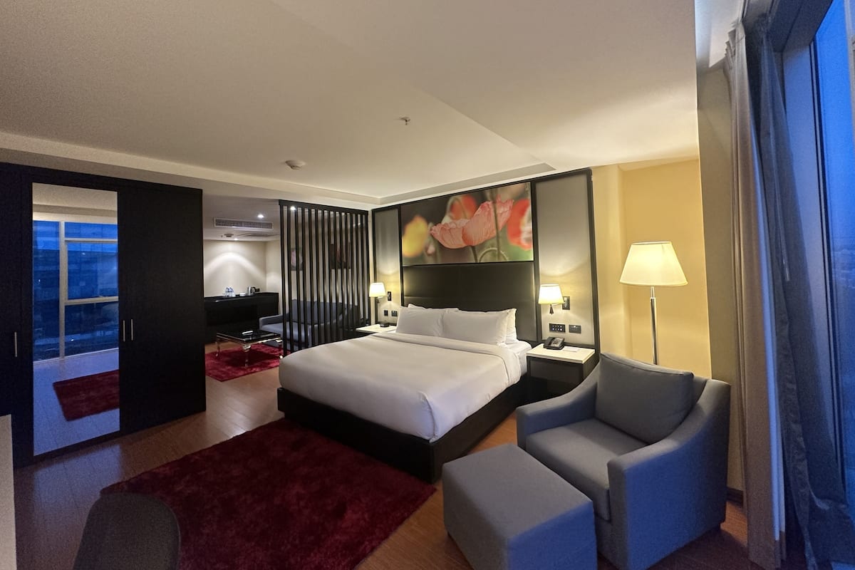 A hotel room with a bed, a chair, a desk, a lamp, and a painting.