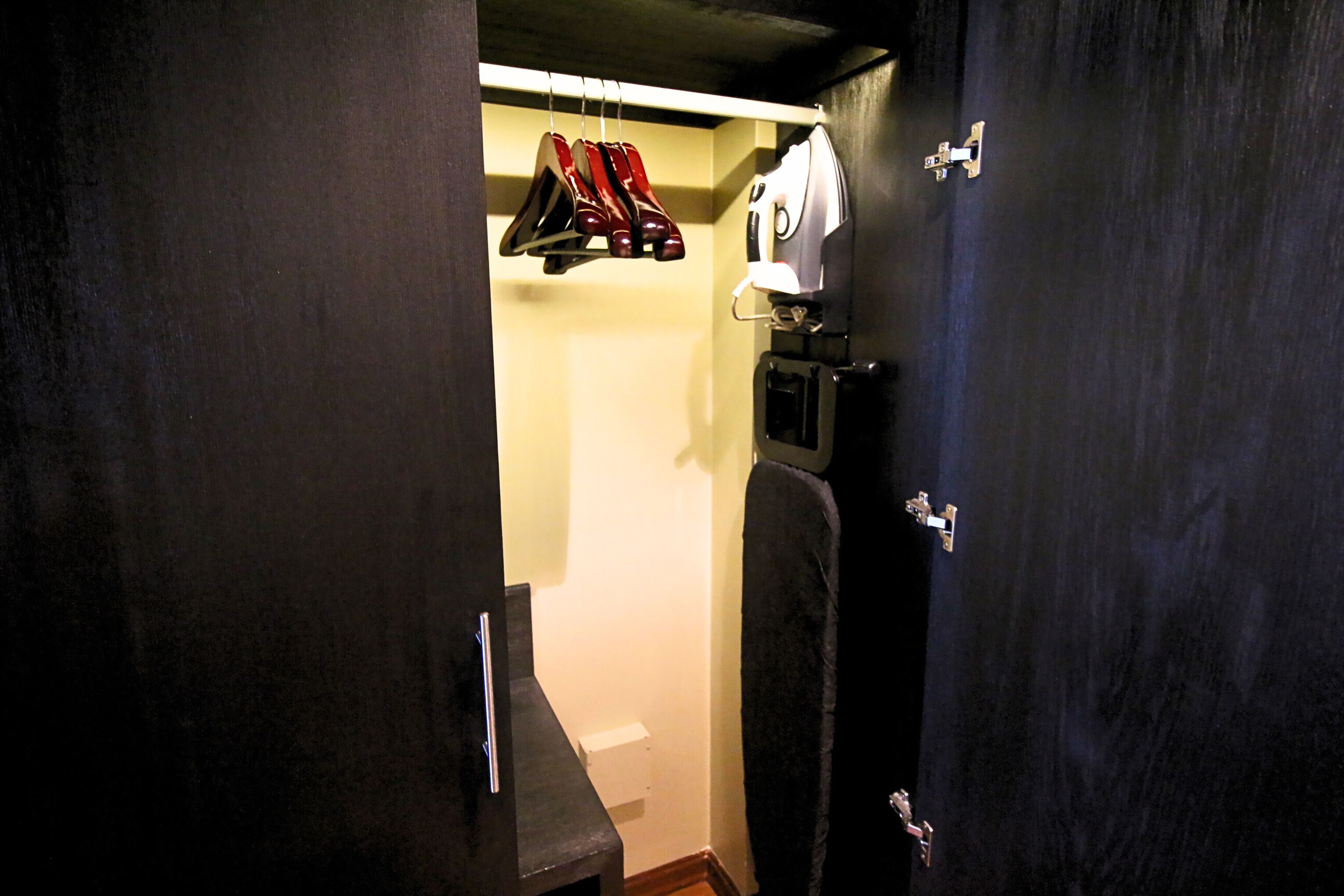 Un pasillo estrecho con una puerta oscura a la derecha, una pared blanca y un perchero con zapatos.