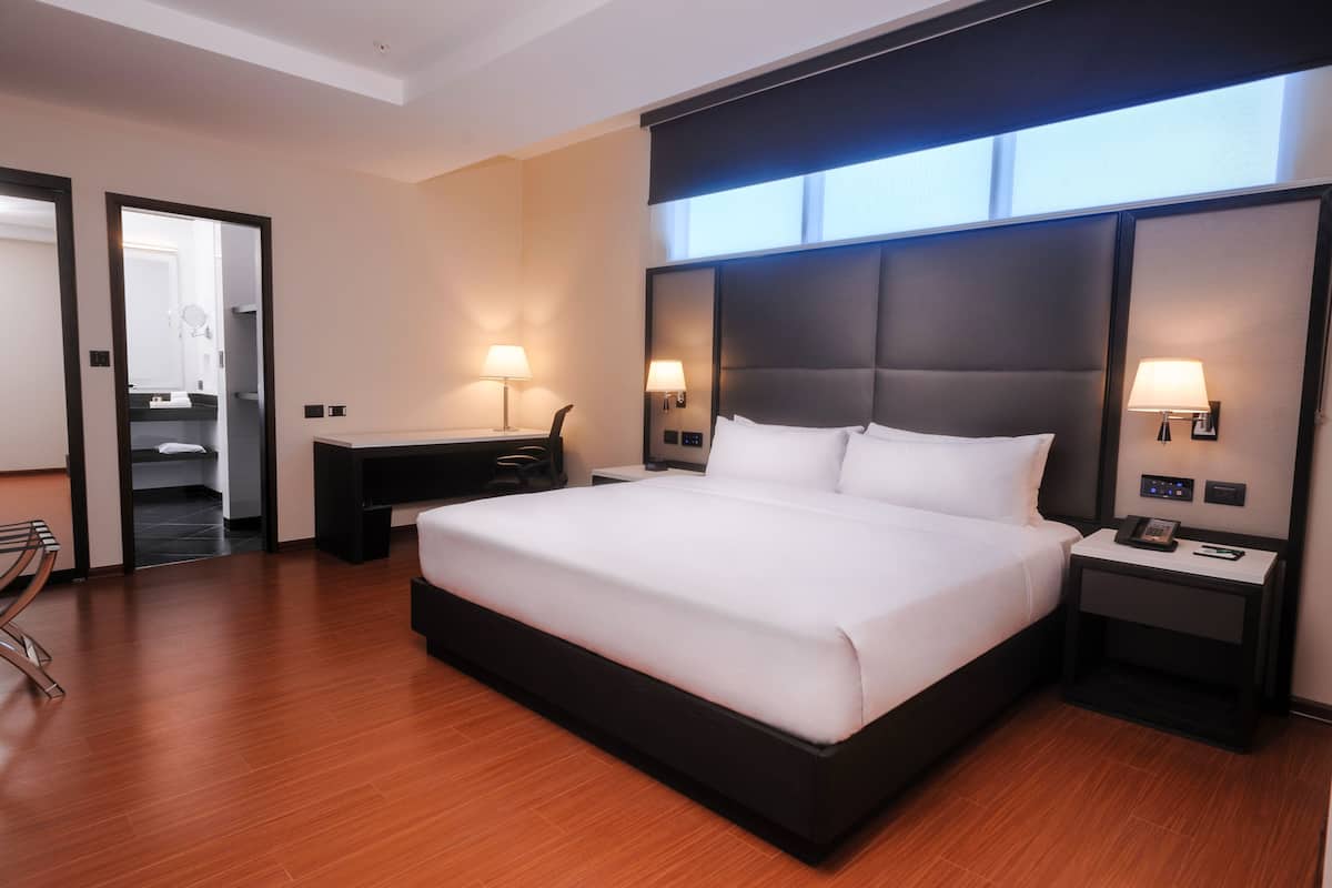 A modern hotel room with a large bed, bedside tables with lamps, a desk, and a chair.