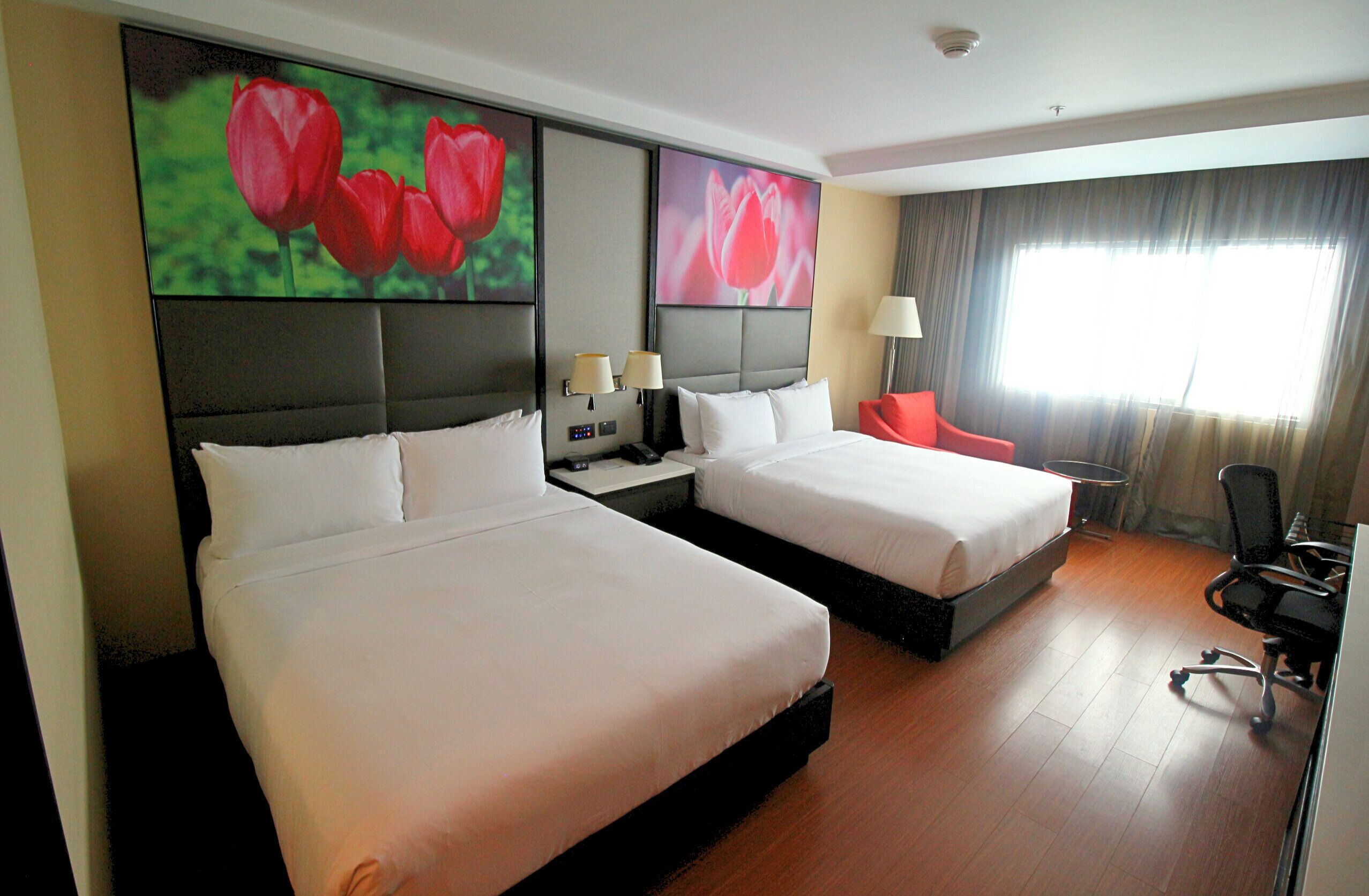 A hotel room with two beds, a desk, a chair, and a large window with curtains.
