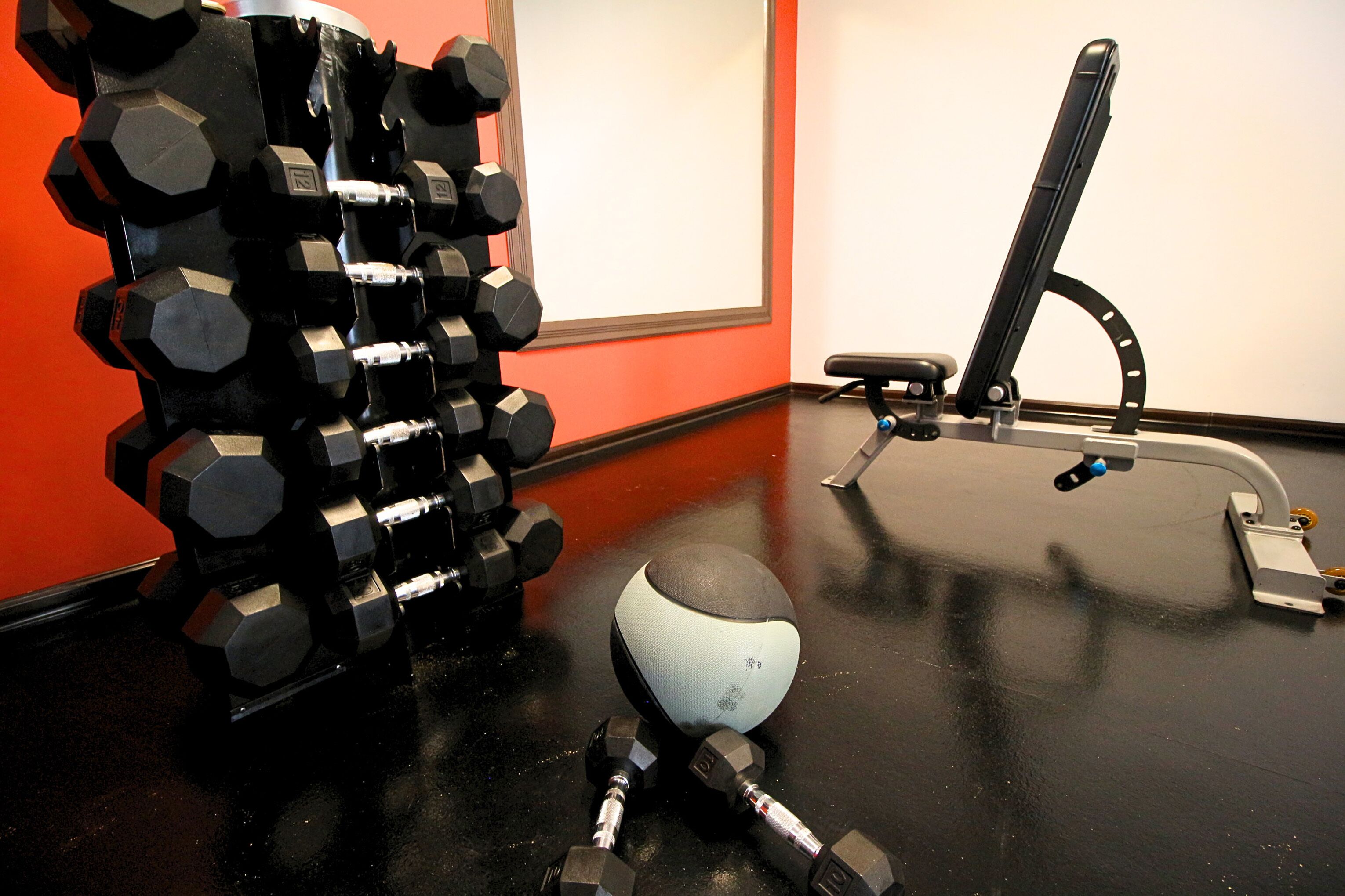 Ein Fitnessraum mit verschiedenen Geräten, darunter Hanteln, Medizinball und eine Trainingsbank.
