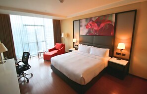 A hotel room with a large bed, a desk, a chair, and a nightstand with lamps.