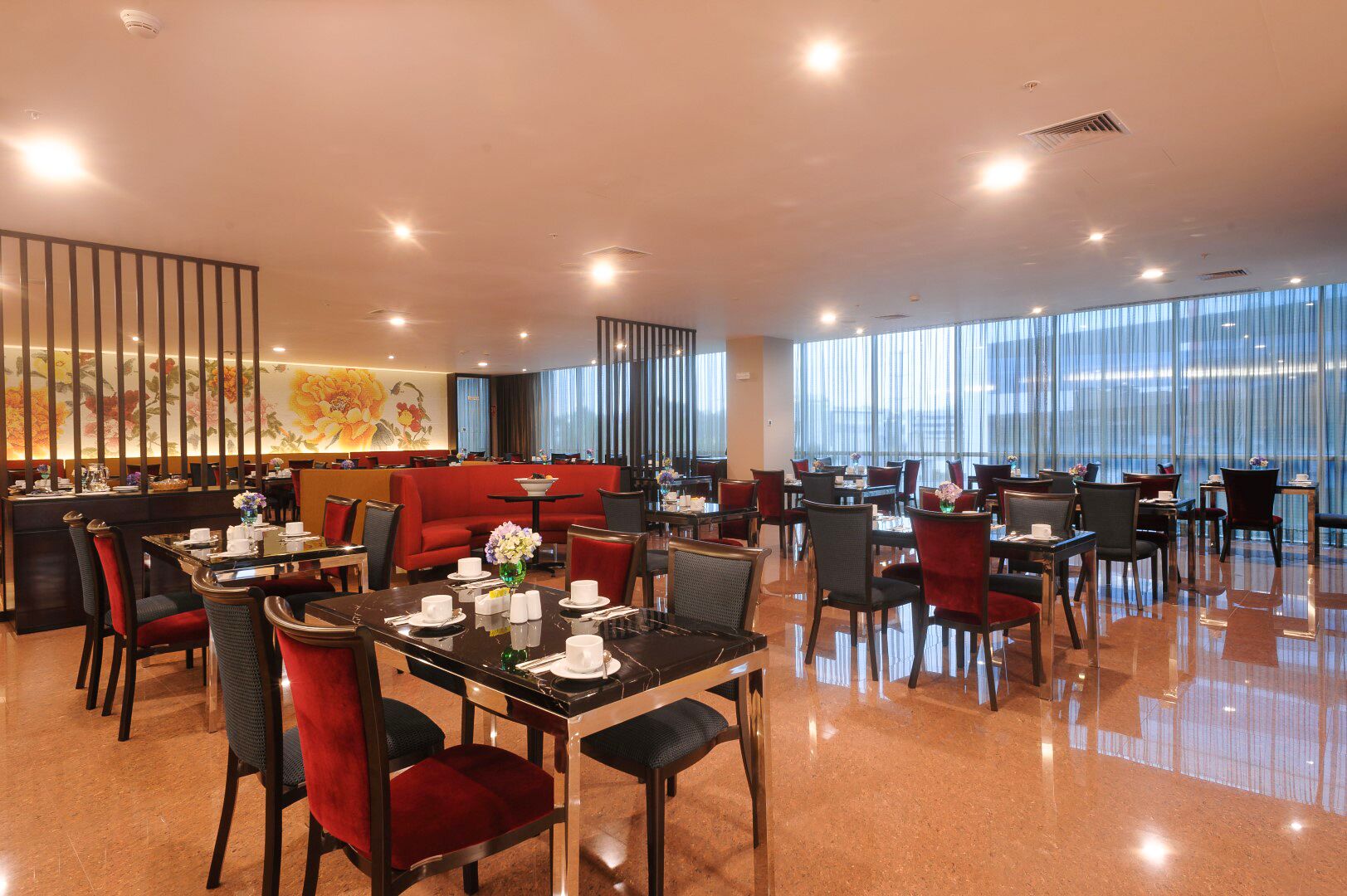 A modern restaurant with a mix of dining areas, including booths and tables, with a red seating area and a large window offering a view.