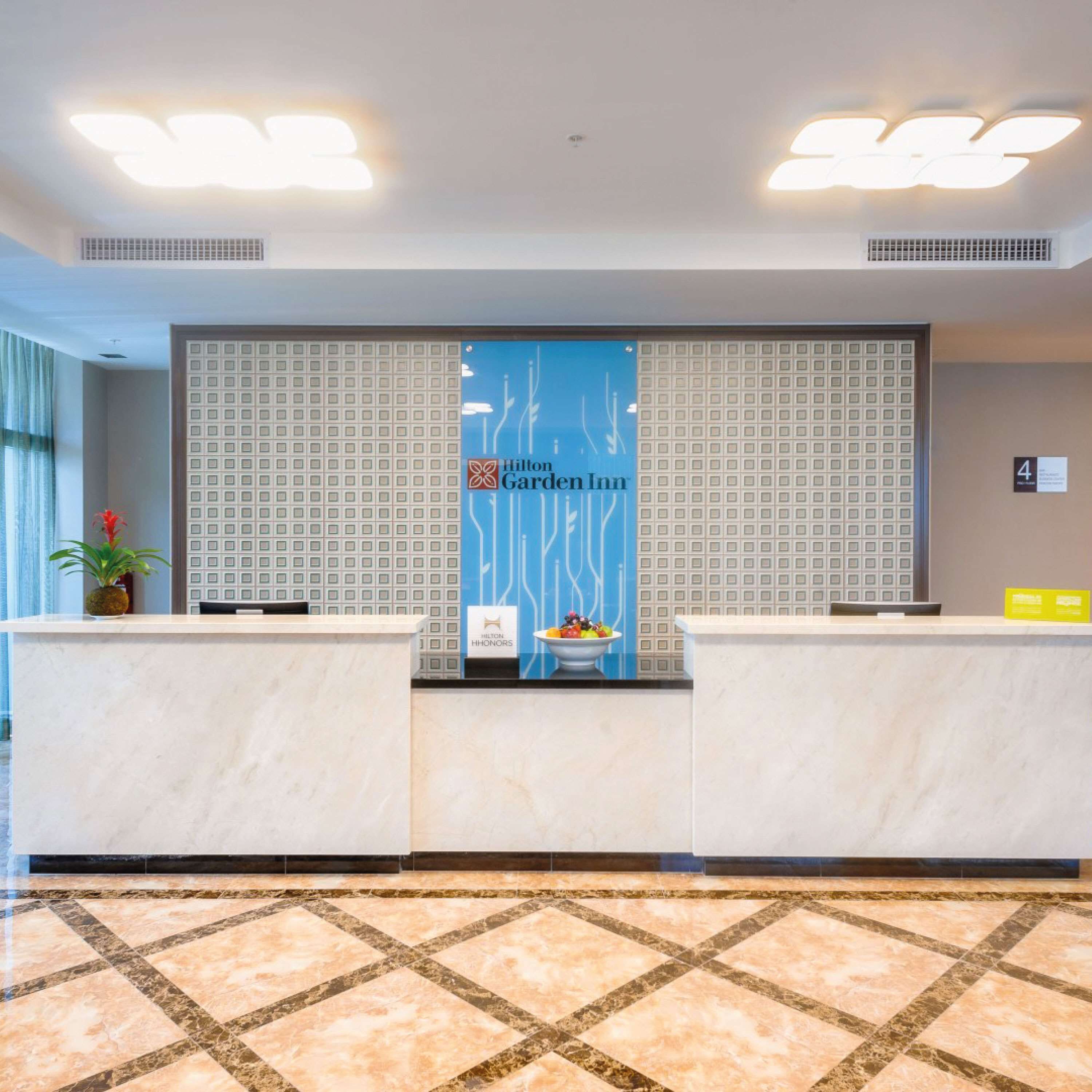 A hotel reception area with a marble counter, a blue wall with the Hilton Garden Inn logo, and a patterned floor.