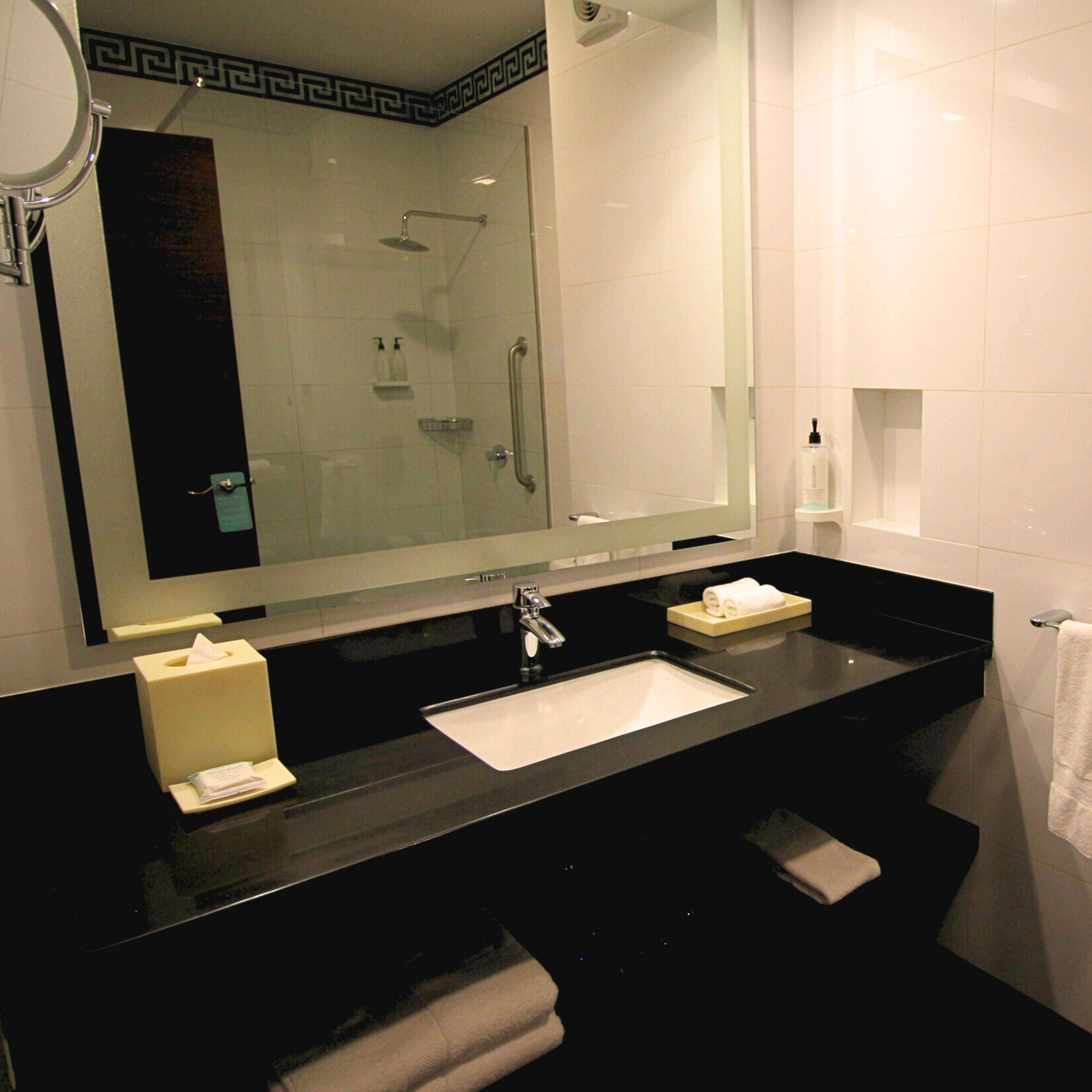 A modern bathroom with a black countertop, a white sink, a large mirror, and a glass-enclosed shower.