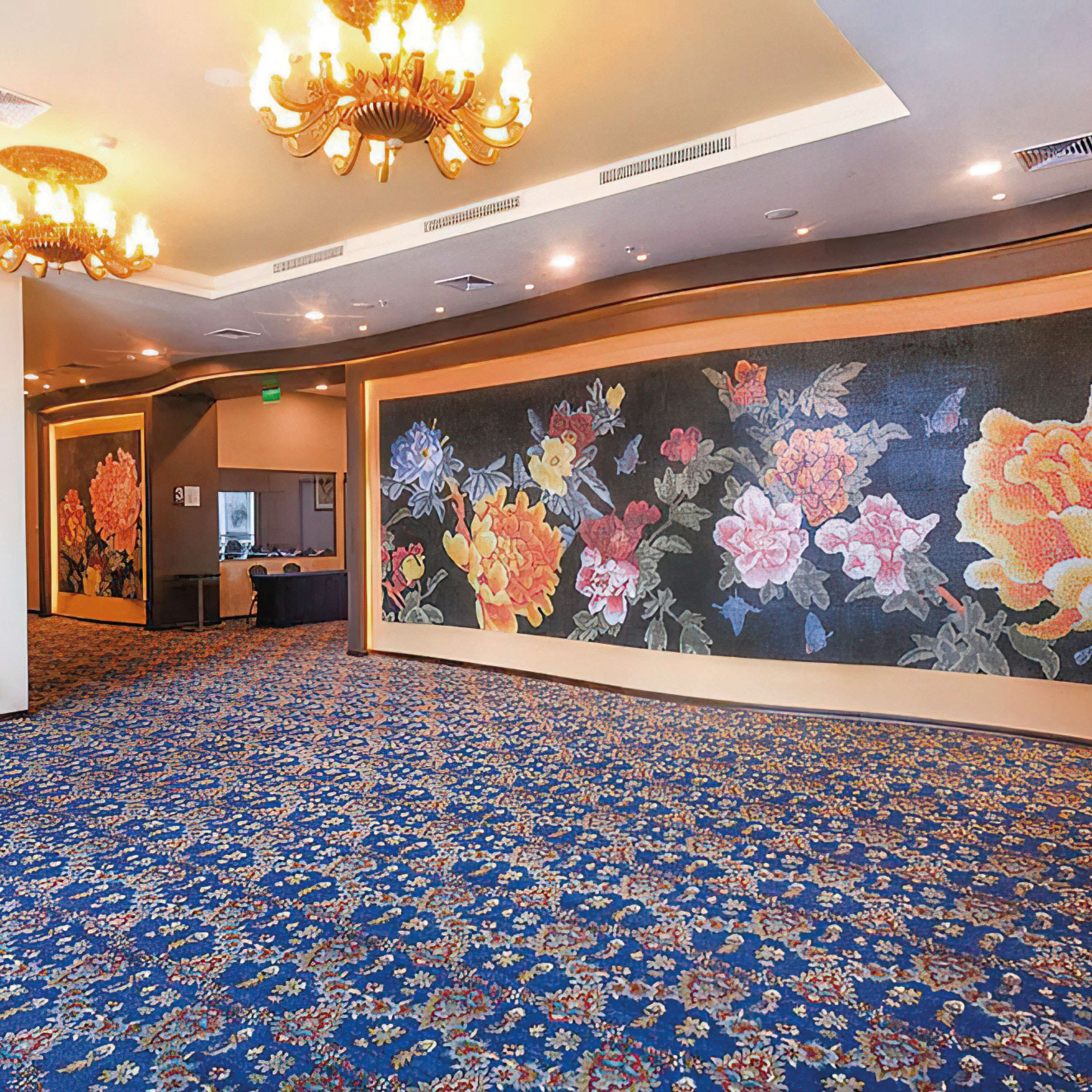 Un hall d’hôtel agrémenté d’une grande fresque florale, d’un lustre et d’un tapis à motifs.