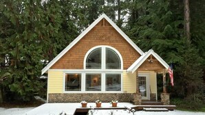 A cabin with a stone foundation, a large arched window, and a flag on the porch. - 01sl - Hot Tub - Pet Friendly - Bbq - Sleeps 8 3 Bedroom Home by RedAwning (Deming)