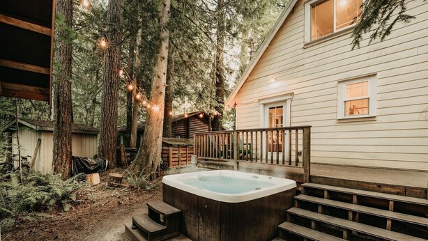 A wooden deck leading to a hot tub with a wooden staircase, surrounded by trees and a wooden cabin. - 01sl - Hot Tub - Pet Friendly - Bbq - Sleeps 8 3 Bedroom Home by RedAwning (Deming)