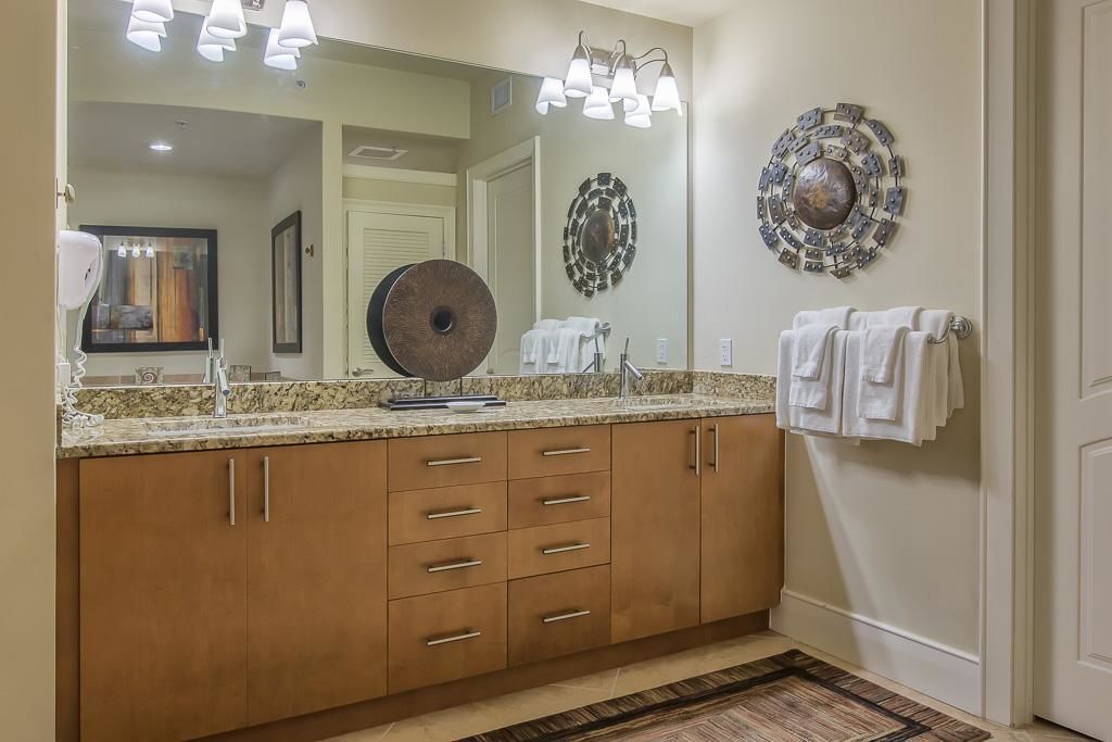 Un baño con un espejo grande, armarios de madera y un adorno de pared estampado.